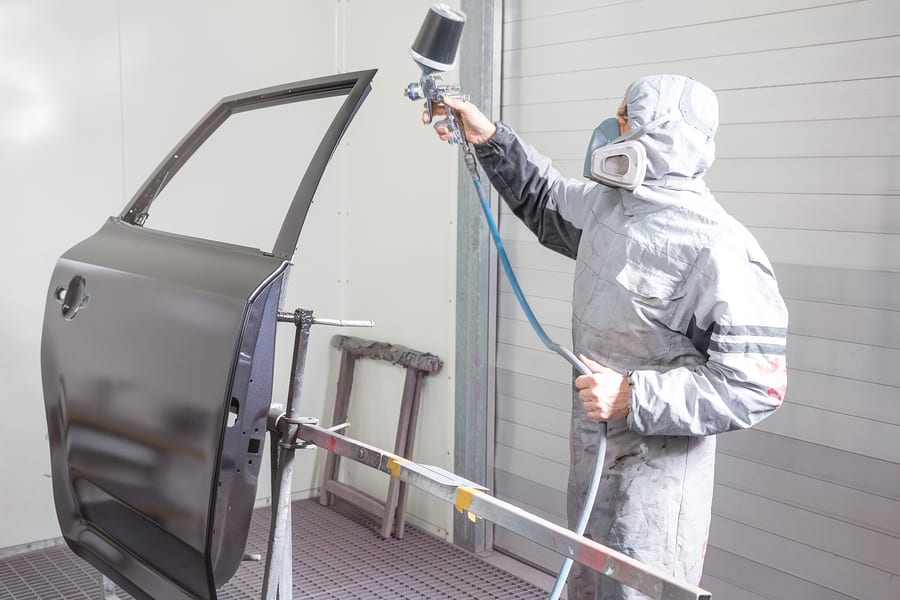 Car body painter spraying paint or color on bodywork in a garage or workshop with an airbrush